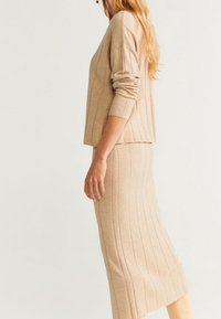 Ensemble en maille beige composé de deux pièces, avec une texture côtelée, un pull à manches longues et une jupe crayon mi-longue avec une légère fente sur le côté.