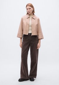 Trumpa, rožinės spalvos odinė striukė su lygia apykakle ir ribuotais rankogaliais, derinama su plačiomis rudos spalvos kelnėmis ir juodais platforminiais batais.