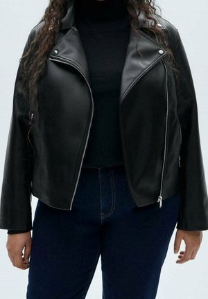 Chaqueta de motorista de cuero negro con cremalleras plateadas, usada sobre un top negro y vaqueros azul oscuro, mostrada desde los hombros hasta las caderas.