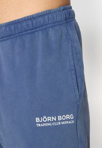 Μπλε φόρμες από μαλακό ύφασμα, με ελαστική μέση και πλαϊνές τσέπες. Περιλαμβάνει λευκά γράμματα στο κάτω αριστερό πόδι.