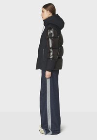 Giacca a vento nera con pannelli spalla lucidi neri, cappuccio e tasche con zip, abbinata a pantaloni di jeans a gamba larga con una striscia grigia.