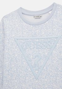 Sudadera de color azul claro con un patrón floral, un logo bordado en forma de triángulo en el centro y un cuello de barco. Textura de tela suave.