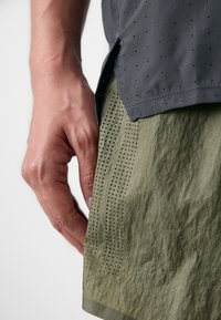 Men's athletic top in dark gray with perforated detailing, paired with olive green shorts featuring textured fabric and ventilation holes.