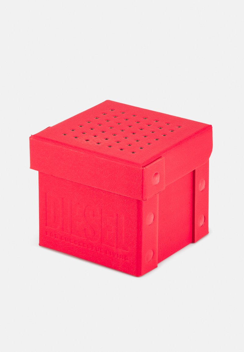 Vörös négyzet alakú doboz, textúrált anyagból készült, perforált tetejével és dombornyomott "DIESEL" logójával, az oldalain kerek szegecsekkel.