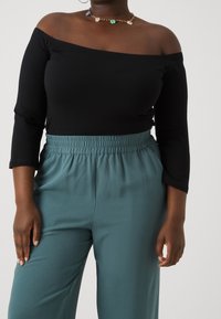 Svart off-the-shoulder topp i kombination med teal elastiska byxor med midjeresår. Inkluderar ett blommigt chokerhalsband i flera färger. Mjuk tygtextur.
