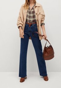 Beige oversized uldblandede cardigan over en ternet skjorte, parret med højtaljede mørkeblå vide jeans og brune læder ankelstøvler.