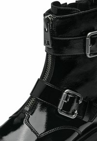 Botín negro de charol con cierre de cremallera, dos correas ajustables con hebillas de metal y un acabado brillante y elegante.