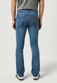 Jeans in denim blu con vestibilità slim, dotati di tasche posteriori con cuciture decorative e una patch in pelle marrone del marchio sul girovita.