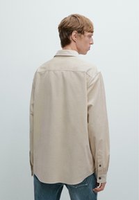 Beige långärmad skjorta med ett subtilt randigt mönster, knäppningar vid ärmsluten och en spetsig krage, matchad med blå jeans.