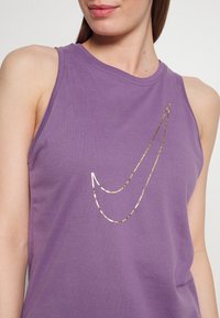 Fioletowy bezrękawnik wykonany z bawełny, z złotym logo Nike w kształcie łyżwy na przodzie, o gładkiej fakturze i okrągłym dekolcie.