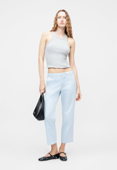 Γυναίκα με αμάνικο crop top σε ανοιχτό γκρι, ανοιχτό μπλε παντελόνι, μαύρες μπαλαρίνες με τρουκς και κρατά μια μαύρη τσάντα χειρός.