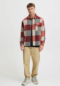 Red and gray plaid flannel shirt with a buttoned front, chest pocket, and a relaxed fit, paired with khaki pants and light sneakers.