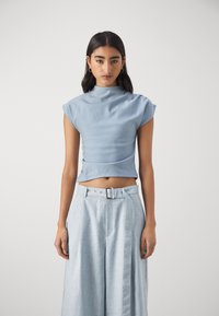 Light blue cropped top with a high neck and short sleeves, paired with light blue wide-leg trousers featuring a side belt and buckle detail.