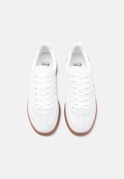 Ζευγάρι λευκά αθλητικά παπούτσια Polo Ralph Lauren με καφέ σόλες, δεμένα με κορδόνια, φαίνονται από πάνω πάνω σε απλή επιφάνεια.