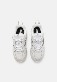 Paire de baskets blanches en mesh avec lacets, vues de dessus sur un fond clair uni.