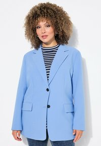 Blazer bleu clair à la coupe ajustée, avec deux poches avant, une fermeture à un bouton noir, et des revers crantés, porté par-dessus un haut rayé.