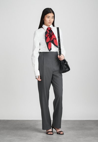 Camisa branca com um lenço padrão vermelho e preto, calças cinzentas de cintura alta e sandálias pretas com tiras. Pequena mala de ombro preta.
