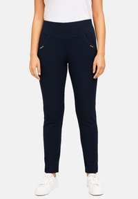 Navy slim-fit leggings with a smooth texture, featuring zippered pockets and a wide waistband, paired with white sneakers.