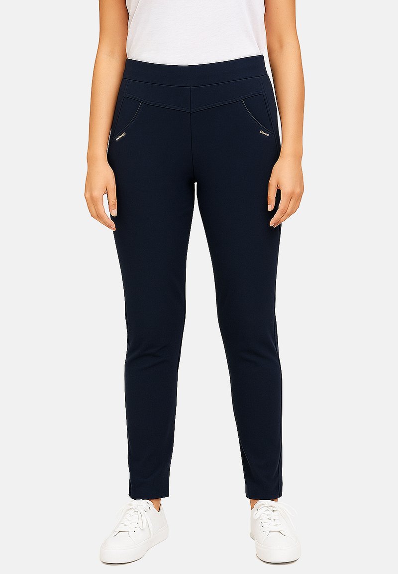 Navy slim-fit leggings with a smooth texture, featuring zippered pockets and a wide waistband, paired with white sneakers.