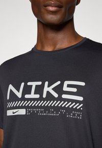 Fekete, rövid ujjú póló fehér "Nike" logóval és szöveges dizájnnal, sima anyagból készült, kerek nyakkivágással és minimális textúrával.