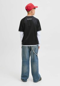 Svart kortärmad skjorta med grå detaljer, i kombination med oversized blå denimjeans som har ett silverkedjetillbehör. Röd keps bärs bakåtvänd.