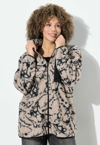 Chlupatá béžová bunda s černými abstraktními vzory, zip na přední straně a elastické manžety. Měkká textura a oversize střih.