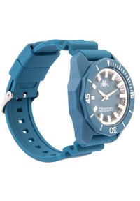 Teal silikonklocka med oktagonal boett, silverdetaljer och en klar urtavla. Har timmarkeringar och en metallspänne.