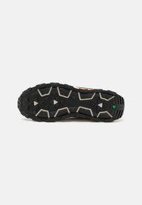 Suela de zapato de goma negra con dibujos angulares, que presenta acentos beige y un punto verde. Diseñada para proporcionar tracción y durabilidad en terrenos ásperos.