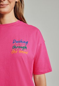 Rosa Baumwoll-T-Shirt mit dem Text "Verwegens durch den Schnee" in mehrfarbigem Stickdesign und einem festlichen Lichterketten-Motiv.