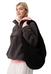 Polarowy pulower w ciemnoszarym kolorze z połową zamka i kieszenią z przodu; warstwowy z jasnoróżową bluzą z kapturem; trzyma czarną pluszową torbę na ramię.