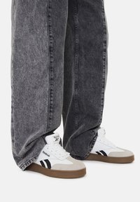 Białe i szare sneakersy Reebok z czarnymi akcentami, w poł�ączeniu z luźnymi, ciemnoszarymi dżinsami. Sneakersy mają gumową podeszwę i są sznurowane.