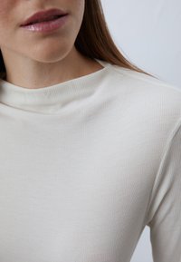 Hellbeige, gerippter Rollkragenpullover mit glatter Textur, hoher Halskrause und figurbetontem Schnitt. Dezenter Glanz des Materials.