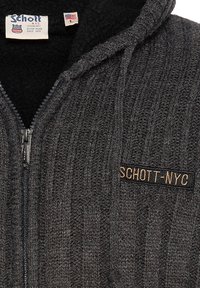 Sweat à capuche gris en maille avec une fermeture éclair, une texture côtelée et une doublure noire. Présente une étiquette cousue "Schott-NYC" en doré sur la poitrine.