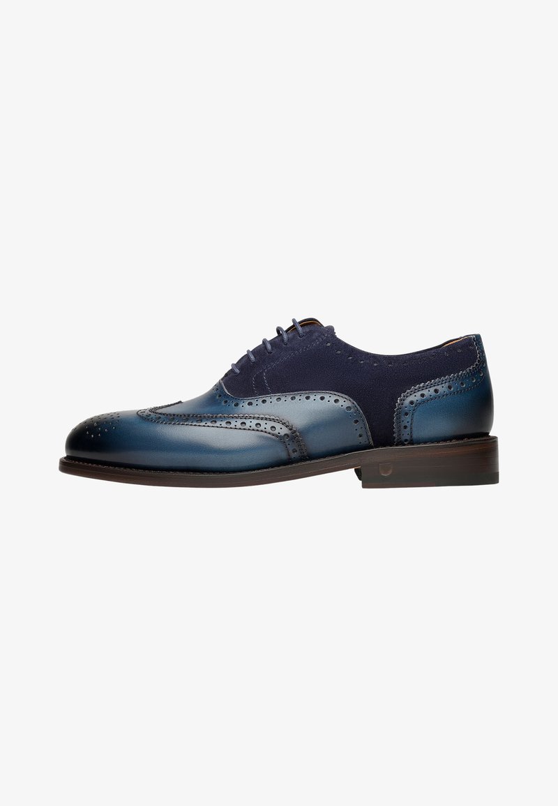 Chaussure habillée en cuir avec une finition dégradée bleue, des détails brogue et des accents en daim marine. Inclut un talon empilé et un système de laçage.