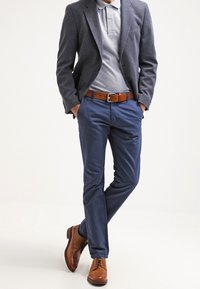 Blazer gris sur un polo gris clair, chinos navy, ceinture en cuir marron et chaussures habillées marron avec des détails perforés.
