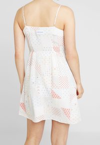 Abito bianco con un motivo a patchwork in rosso e blu, caratterizzato da spalline sottili e una vita arricciata. Etichetta visibile sul retro.