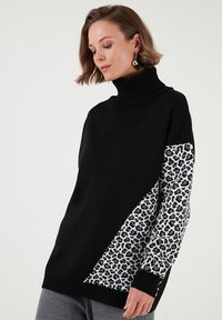 Pulover negru cu guler înalt, având un panou diagonal cu imprimeu leopard alb și negru pe un mănunchi. Textură moale, croială lejeră.