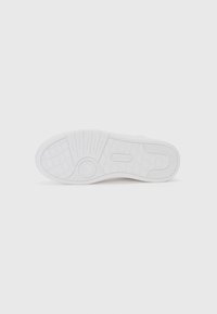 Hvit sneakersåle med teksturert gummi, med et sirkulært akcent og skrå linjer for grep. Minimalistisk design med logo.