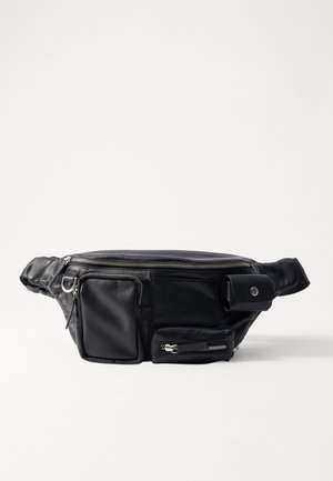 Crna kožna torbica oko struka s više zip kompartmana, ravnim prednjim džepom i teksturiranom površinom. Sadrži metalne aksentne detalje.