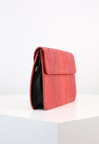 Červená texturovaná kabelka na ruku se vzorem hadí kůže, má černý interiér a uzávěr na klopě. Design je obdélníkový a jednoduchý.