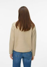 Felpa beige con maniche lunghe, polsini a coste e orlo arrotondato, abbinata a jeans in denim blu. Tessuto morbido e strutturato in vista.