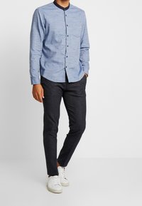Ljusblå långärmad skjorta med knapprad, marinblå krage och bröstficka, tillsammans med mörka slim-fit byxor och vita sneakers.