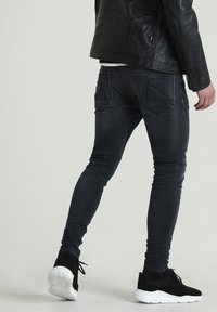 Jeans ajustados negros con un acabado desgastado, diseño de cinco bolsillos y un exclusivo bordado en el bolsillo trasero, combinados con unas zapatillas de ante negras y una chaqueta de cuero negra.
