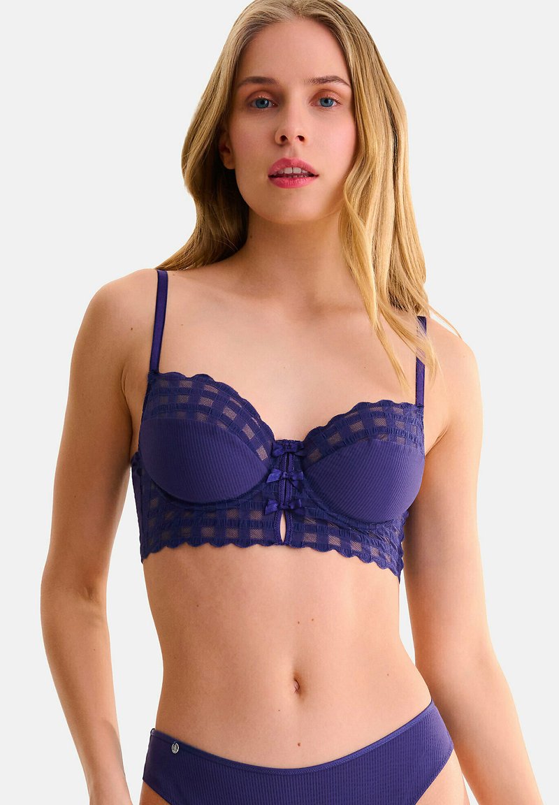 Soutien-gorge violet en tissu ribbé avec des détails en dentelle. Présente des bonnets structurés, des bords festonnés et un petit détail en forme de trou de serrure à l'avant.