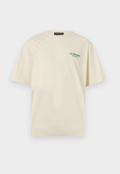 T-shirt en coton couleur crème à manches courtes, avec un logo vert imprimé sur la poitrine gauche. Coupe décontractée et col rond.