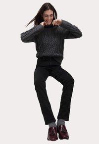 Suéter de punto gris con cuello alto, jeans negros, calcetines grises y mocasines burdeos con borlas. Textura suave y corte relajado.