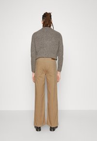 Pull en maille gris avec un col rond, associé à un pantalon ample marron clair. Le pantalon comporte des poches arrière et des passants pour ceinture.