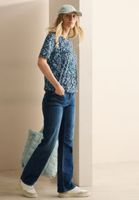 Top corto a maniche corte con fantasia blu, jeans blu scuro, sneakers bianche e una tote bag trapuntata blu chiaro; design minimalista, stile casual.