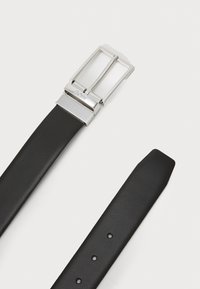 Ceinture en cuir noir avec une boucle en métal argenté. La ceinture présente une texture lisse, plusieurs trous d'ajustement et une extrémité effilée.