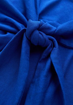 Blåt bomuldsstof med en knude i midten, glat tekstur og let udstrakte områder, der skaber en samlet effekt omkring knuden.